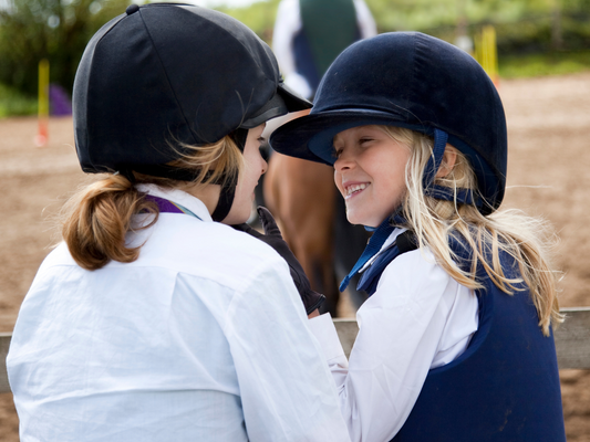 Two young riders wearing helmet smile, ready to take on Pony Finals